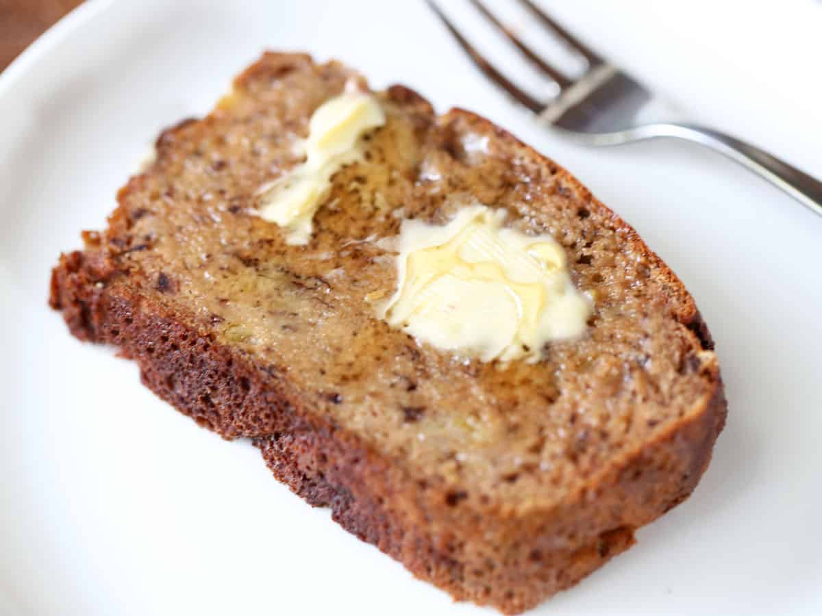 A buttered banana bread slice on a plate.