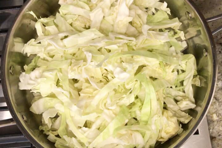 Placing the shredded and rinsed cabbage in a deep skillet.