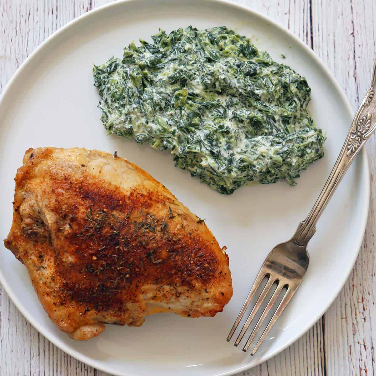 Skin-on, bone-in chicken breast is served with creamed spinach.