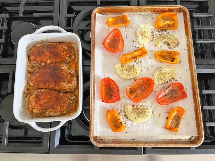 A pan of baked chicken breasts next to a pan of roasted peppers and onions.