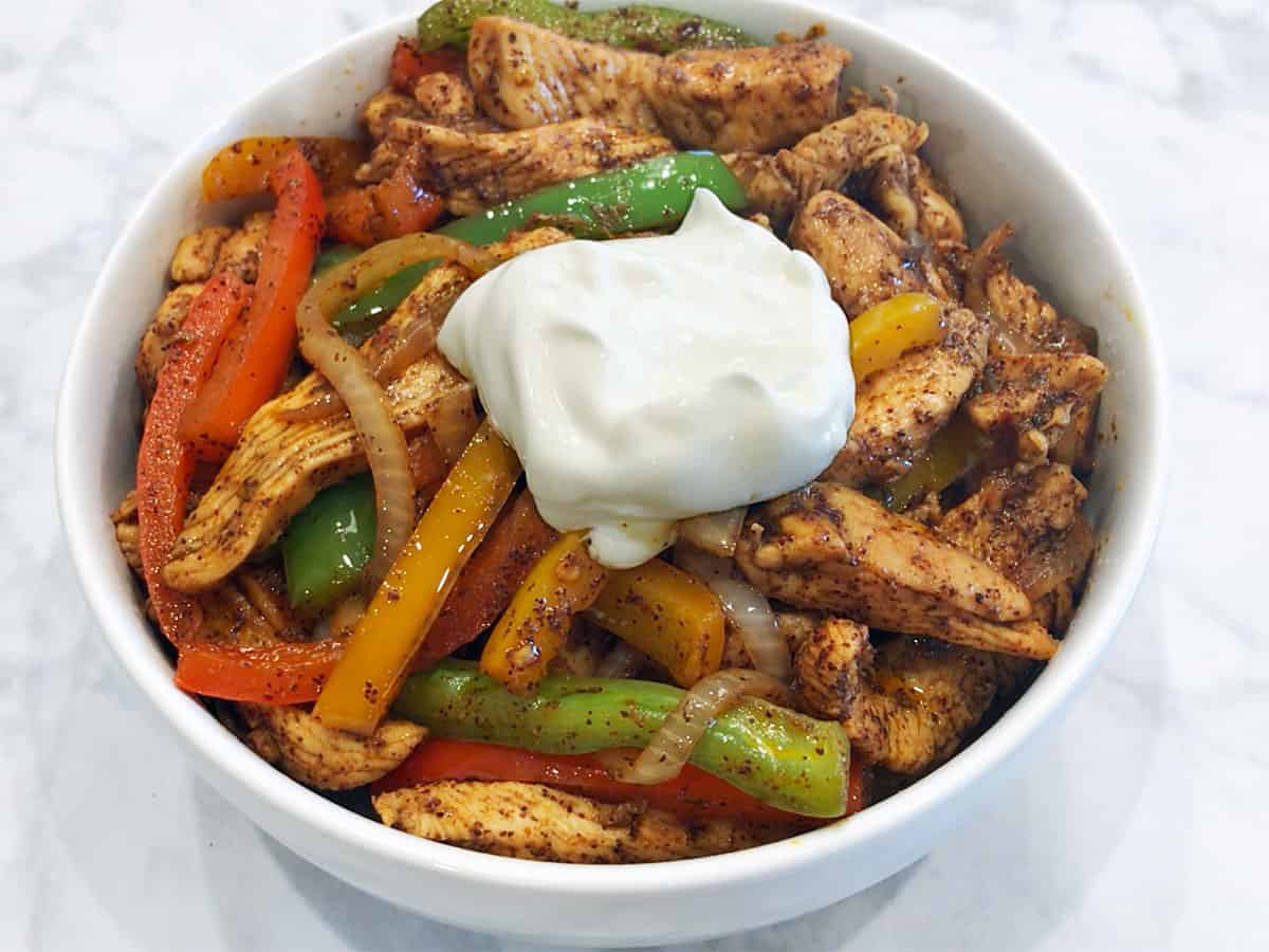 Chicken fajitas are served in a bowl, topped with sour cream.