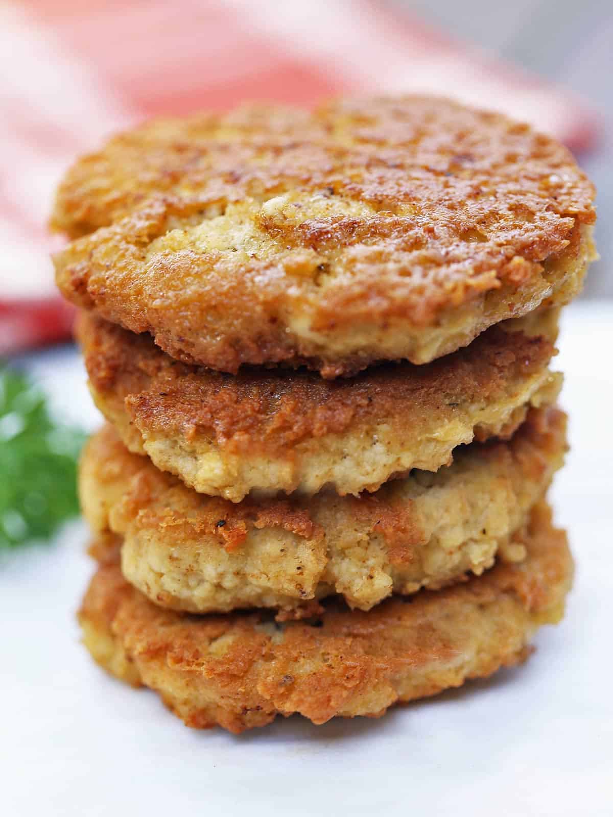 Four chicken patties are stacked on a plate.