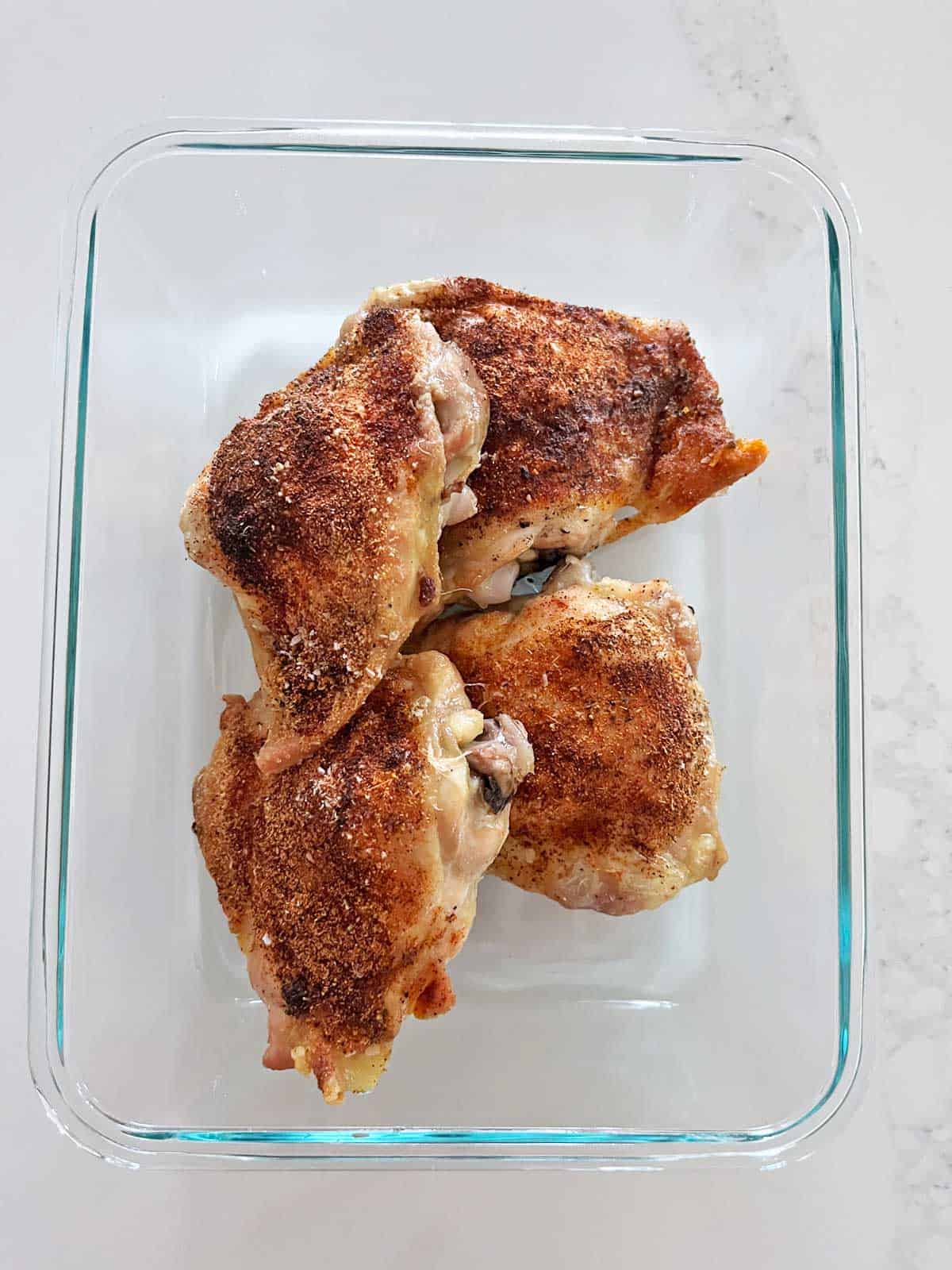 Storing leftover baked chicken thighs in a glass food storage container.