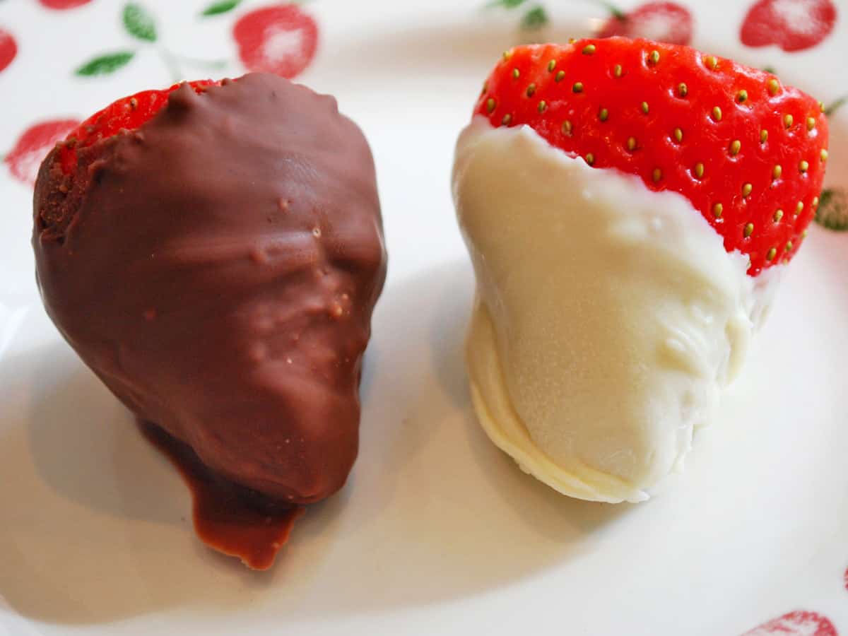 Two strawberries on a plate, one covered in milk chocolate and one in white.