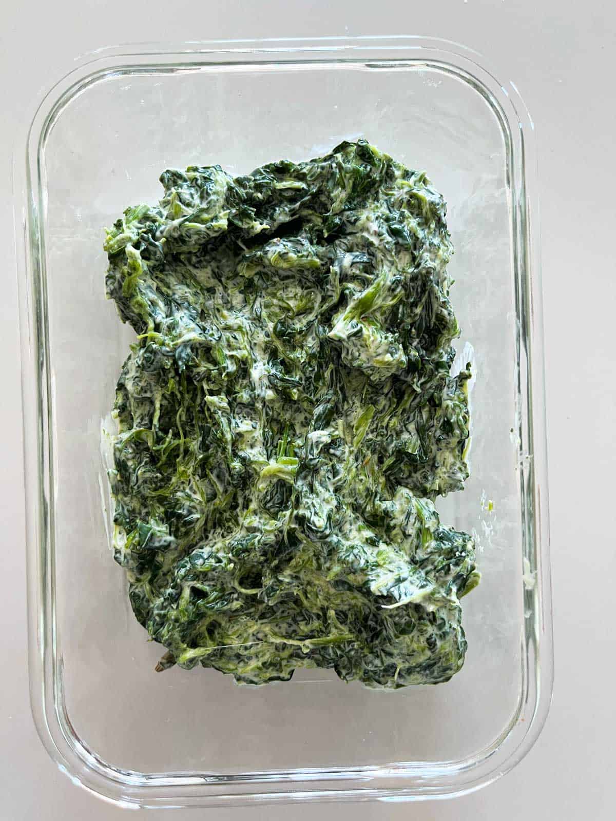Leftovers of creamed spinach are stored in a glass food storage container.