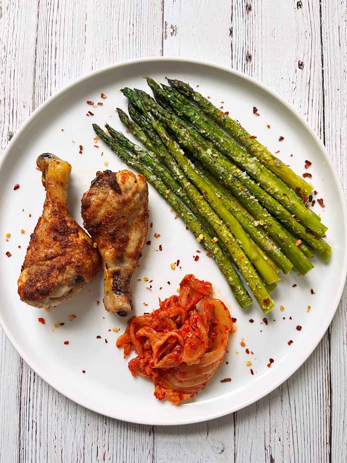 Baked chicken drumsticks are served with roasted asparagus and kimchi.