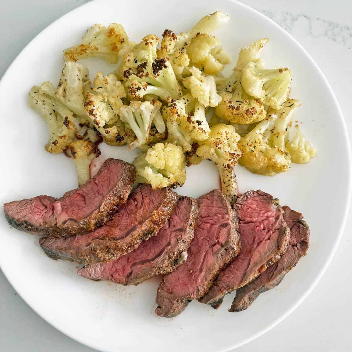Sliced flat iron steak is served with roasted cauliflower.