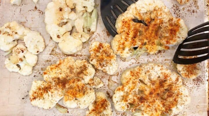 Flipping the cauliflower steaks with two wide spatulas.