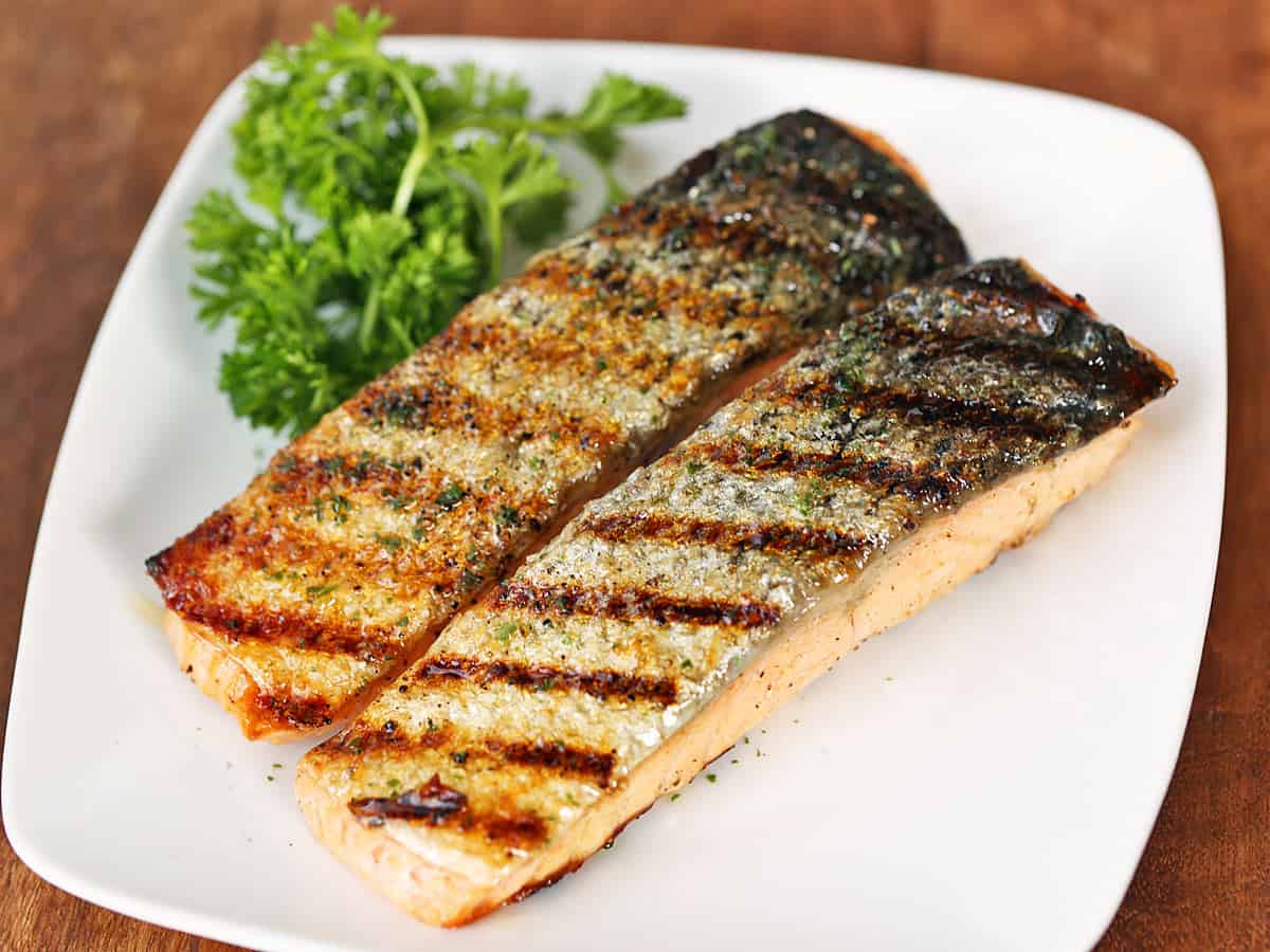 Two grilled salmon fillets on a plate, skin side up.