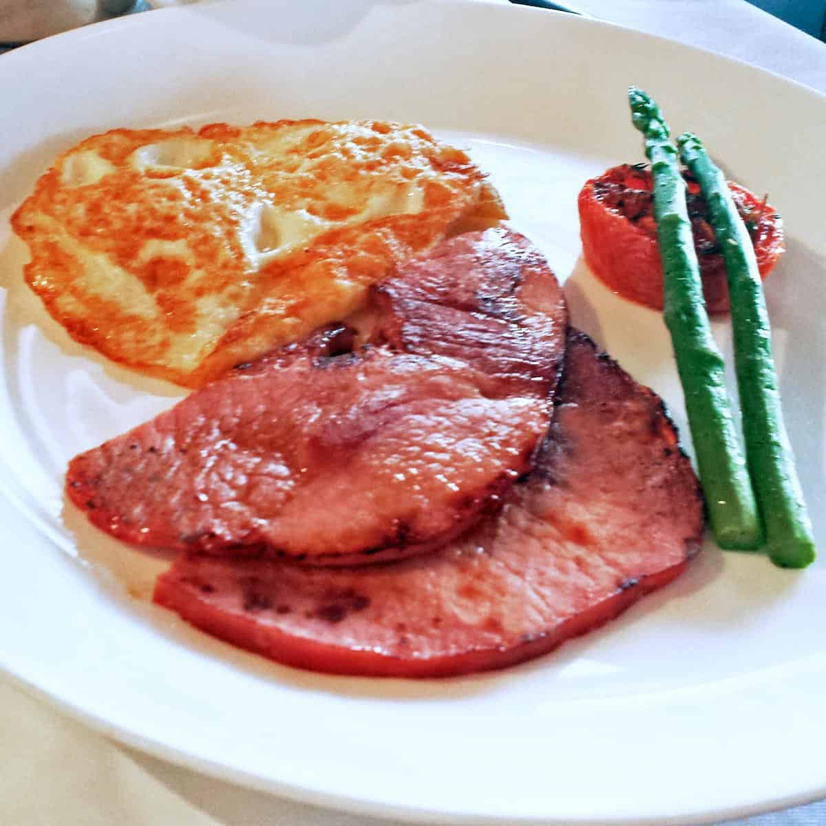 Ham steaks are served for breakfast with fried eggs, a broiled tomato, and steamed asparagus.