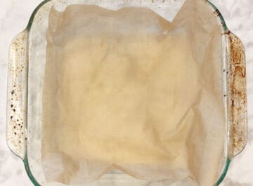 A square baking dish is lined with parchment paper.