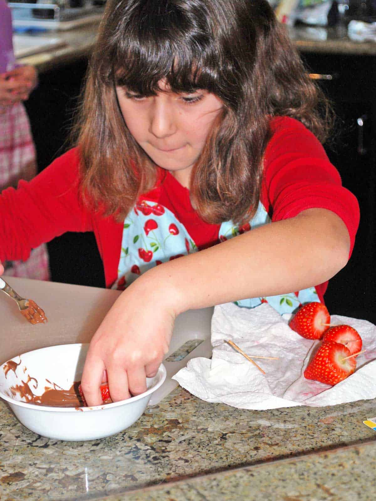 Vered's young daughter dipping a strawberry into a bowl of melted chocolate.