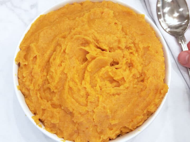 The mashed sweet potatoes are served in a white bowl with a serving spoon.