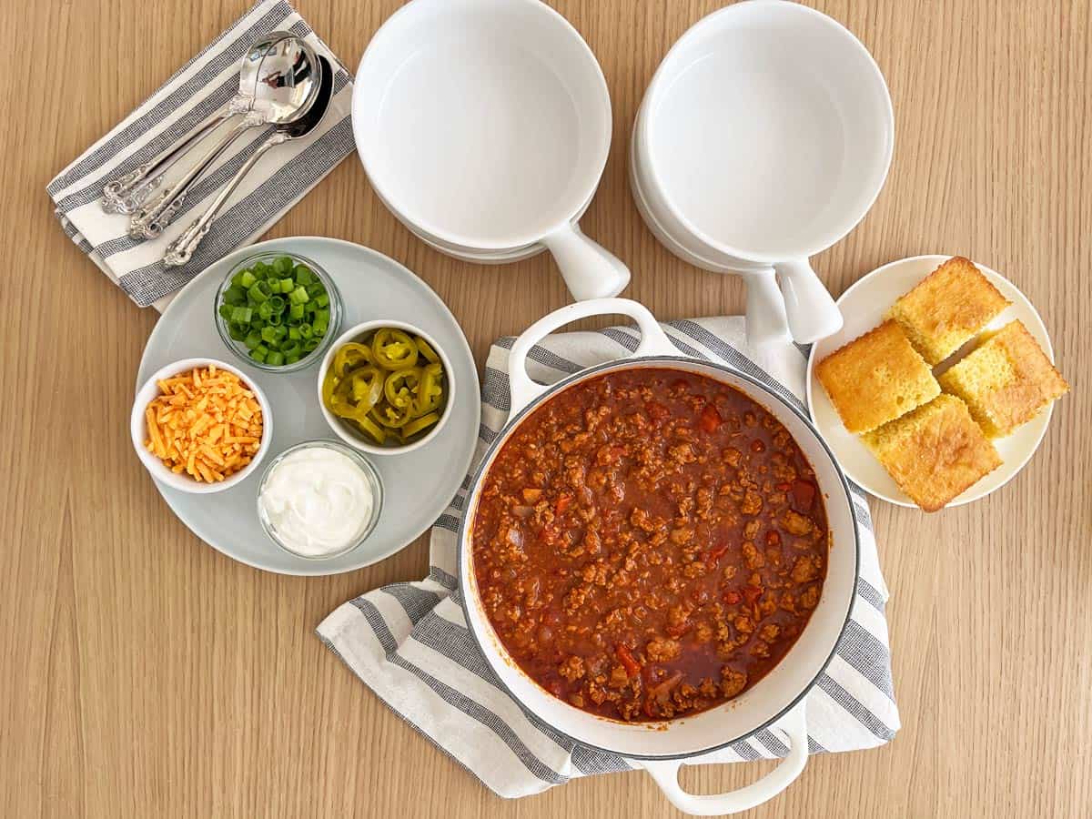 No-bean chili in a white saucepan surrounded by serving bowls and toppings.