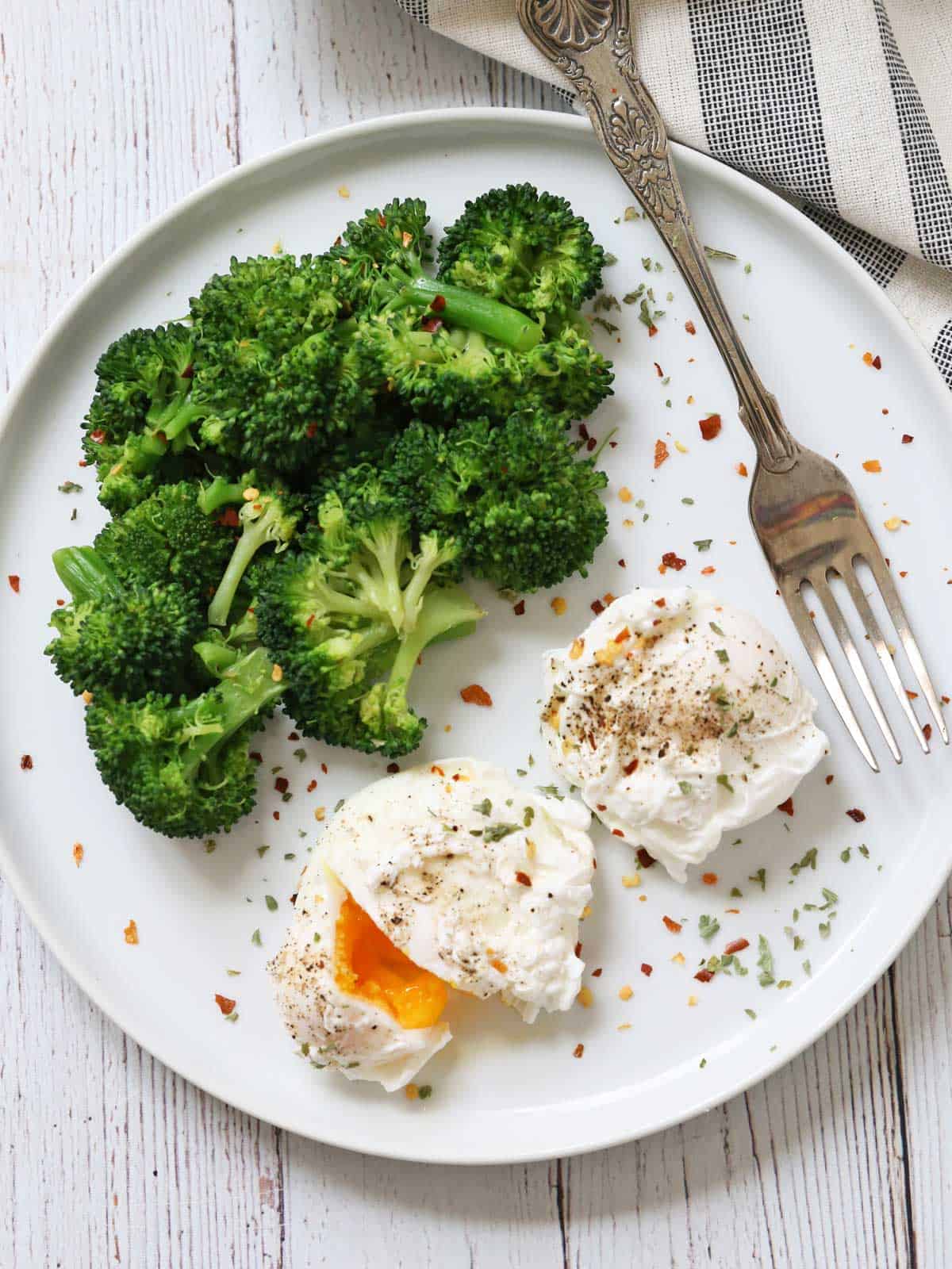 Microwave broccoli and two poached eggs on a plate with a fork.