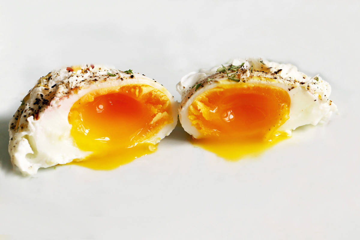 A closeup of a cut poached egg, showing off its thick, jammy yolk.