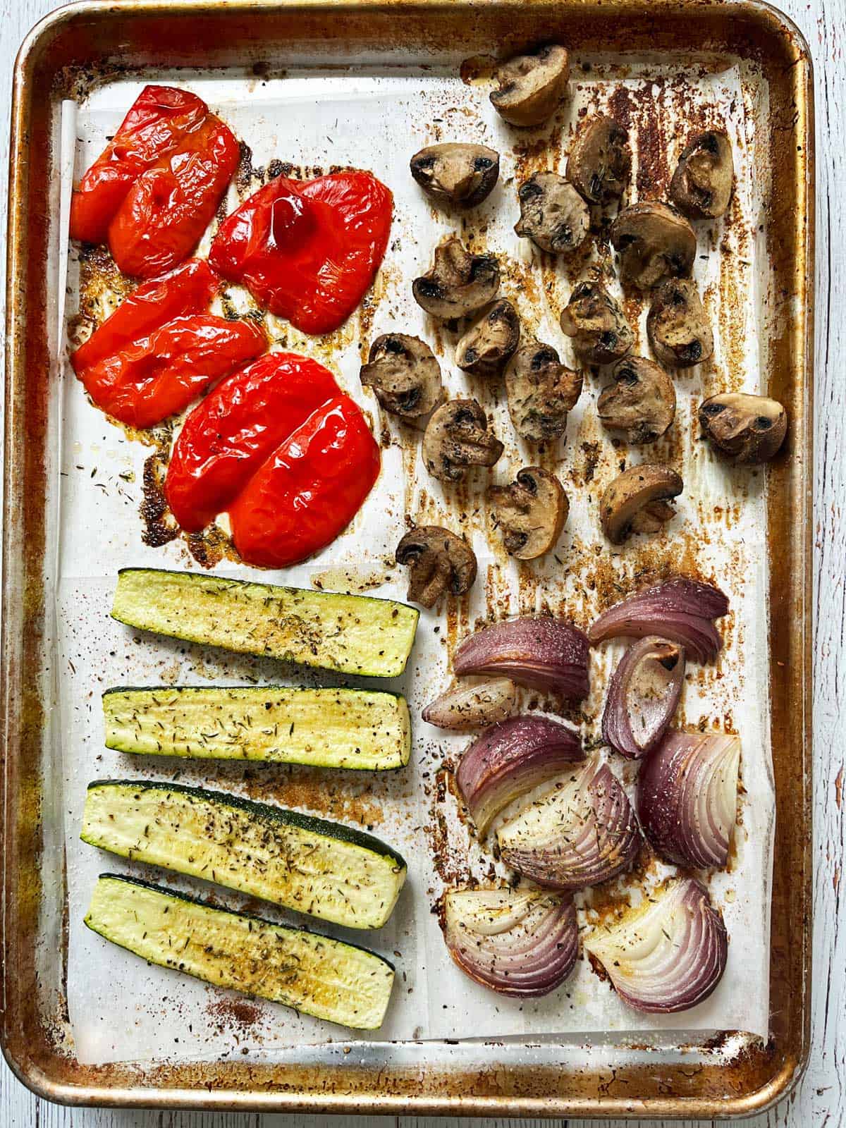Roasted zucchini, red onion, bell pepper, and mushrooms on a sheet pan.