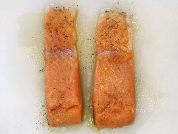 Two seasoned salmon fillets on a cutting board.