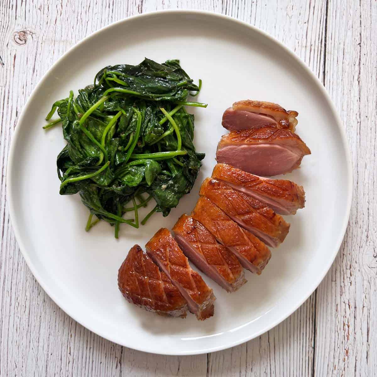 A sliced duck breast is served with sauteed spinach.