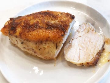 Sliced skin-on chicken breast on a plate.