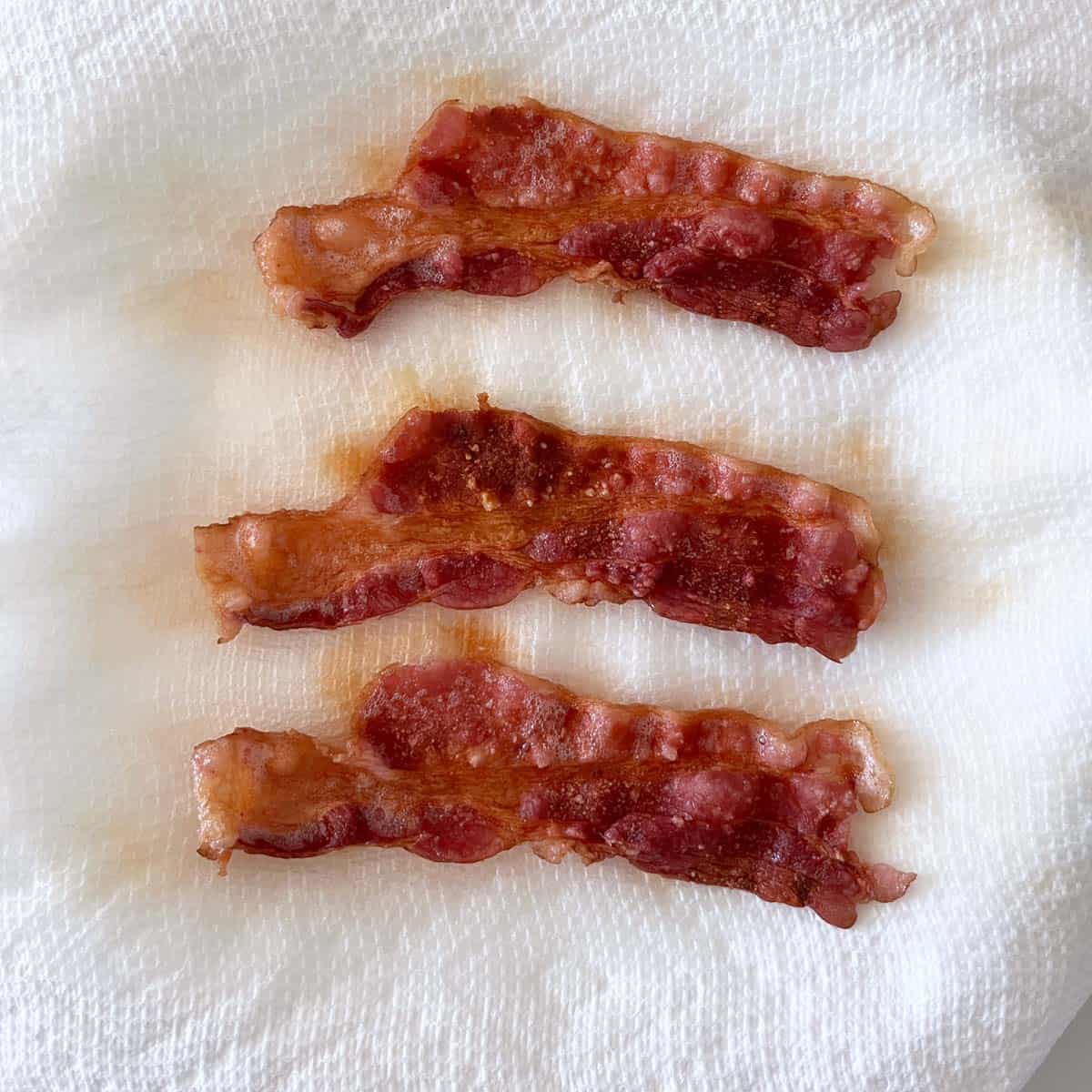 Three slices of bacon that were microwaved for three minutes are came out crispy.