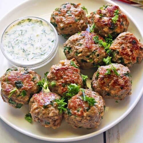 Lamb meatballs are served on a white plate with a yogurt dip.