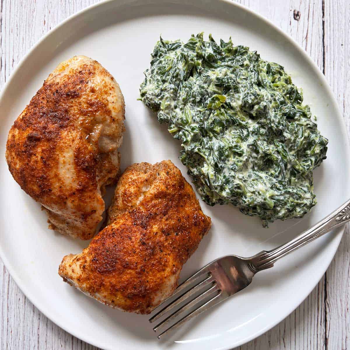 Two boneless chicken thighs are served with creamed spinach.