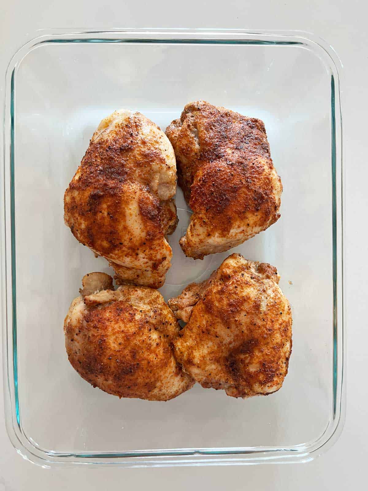 Boneless chicken thighs leftovers are stored in a glass food storage container.