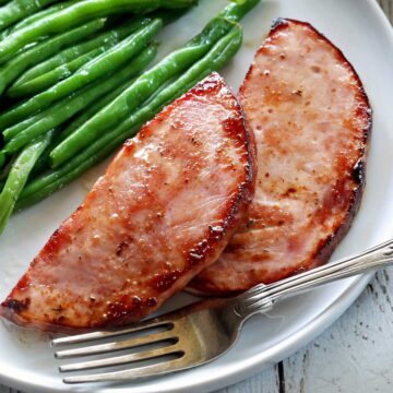 Ham steak is served with green beans.