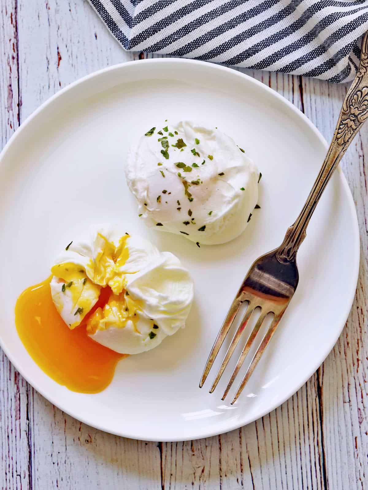 Two poached eggs on a plate with a fork.