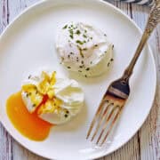 Two poached eggs are served on a plate with a fork.