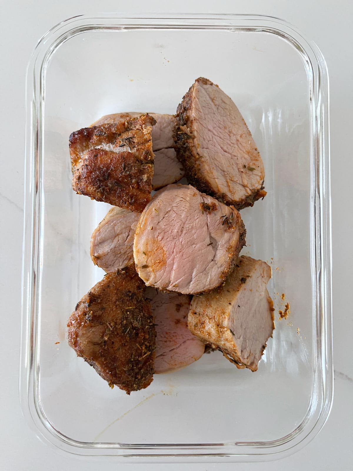 Leftover sliced pork tenderloin is kept in a glass food storage container.