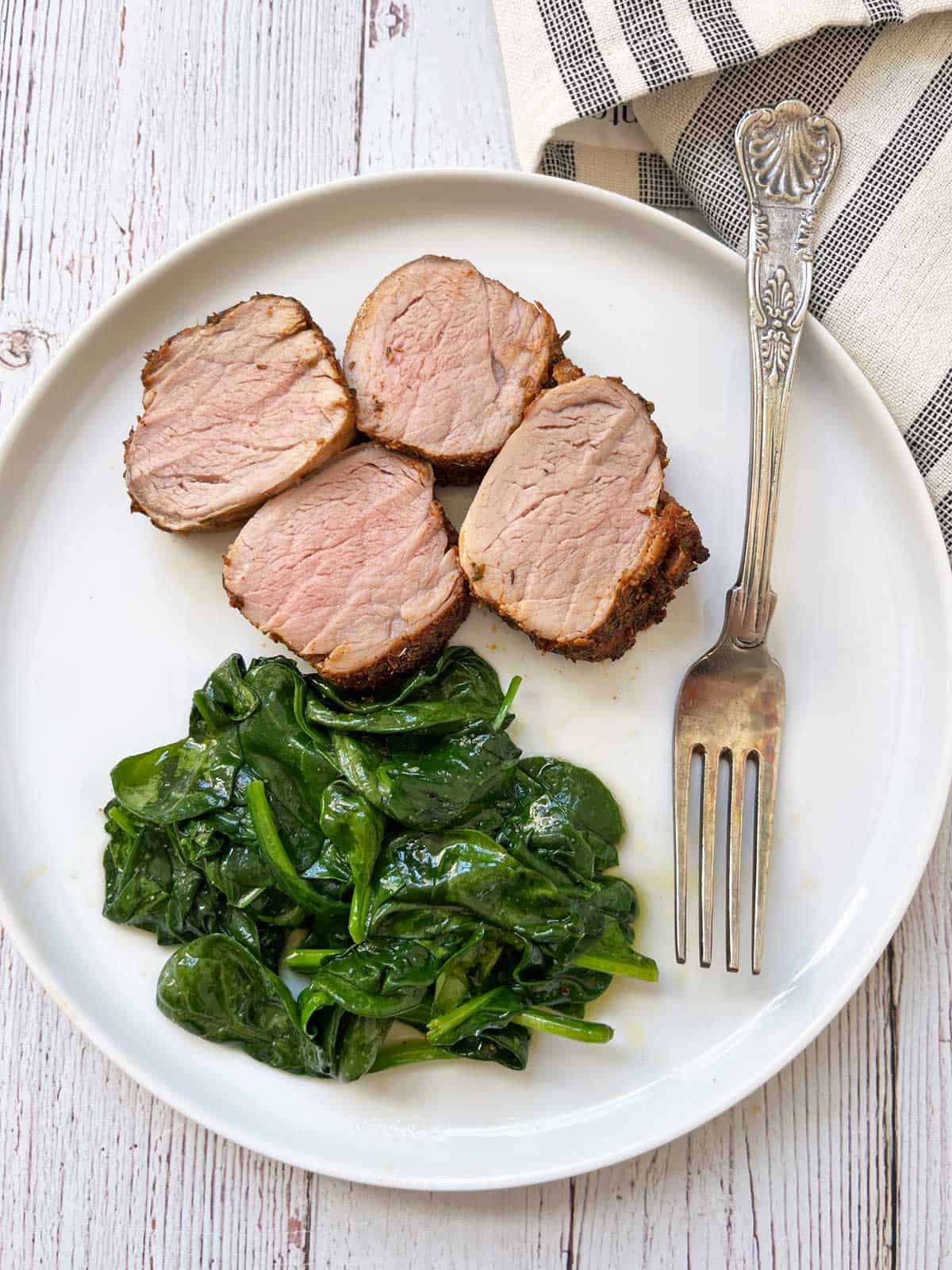 Slices of roasted pork tenderloin are served with sauteed spinach.