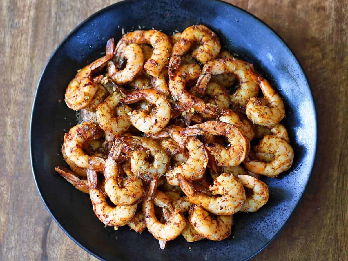 Tail-on spicy shrimp are served on a plate.