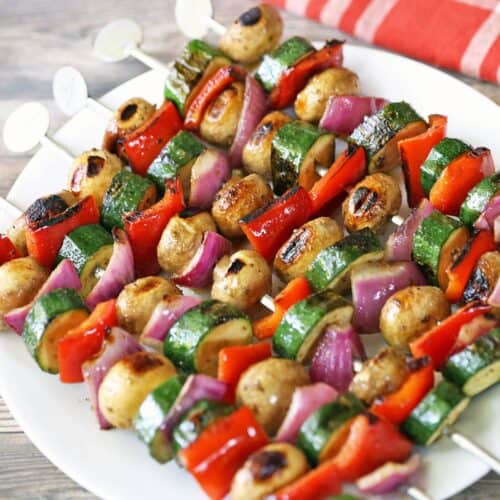 Veggie kabobs are served on a white plate with a napkin.