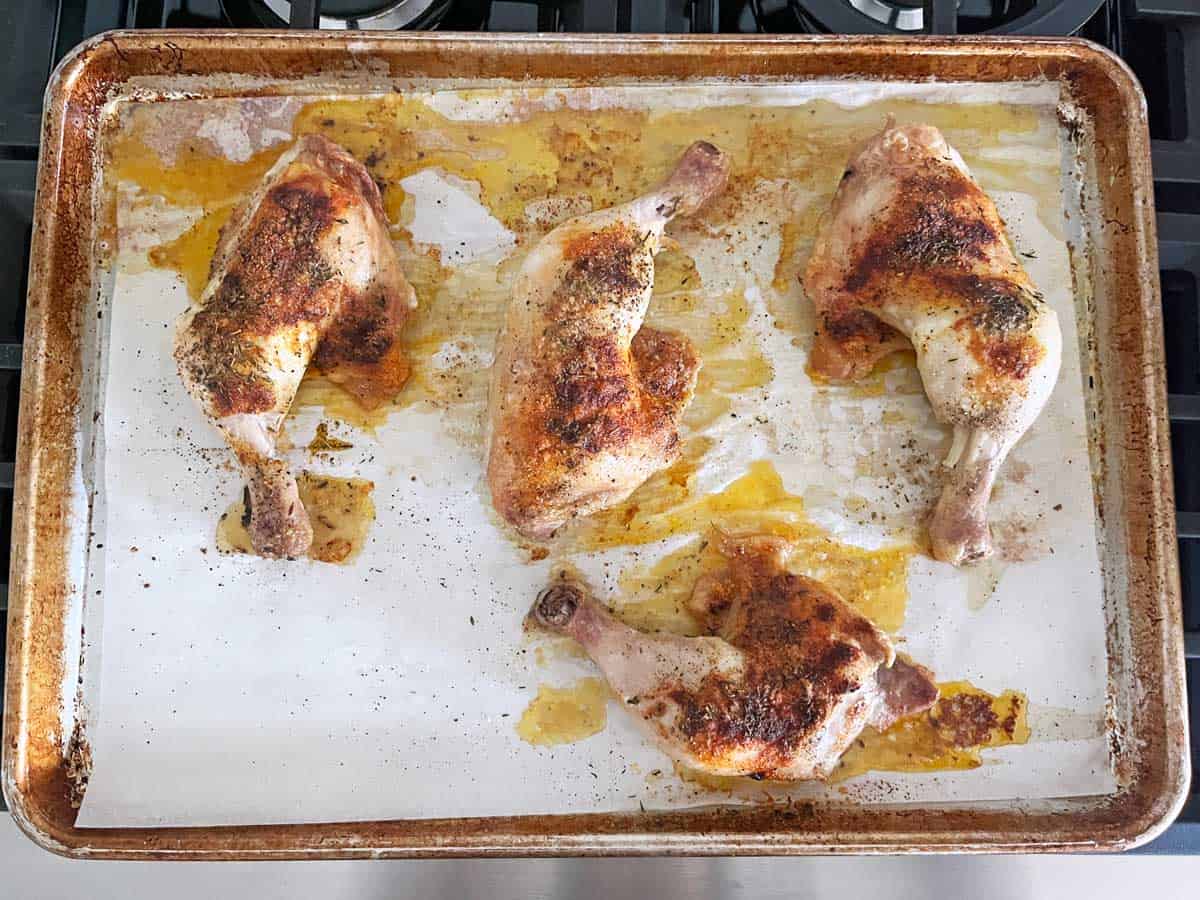 Four chicken leg quarters in the baking sheet after 30 minutes in the oven.