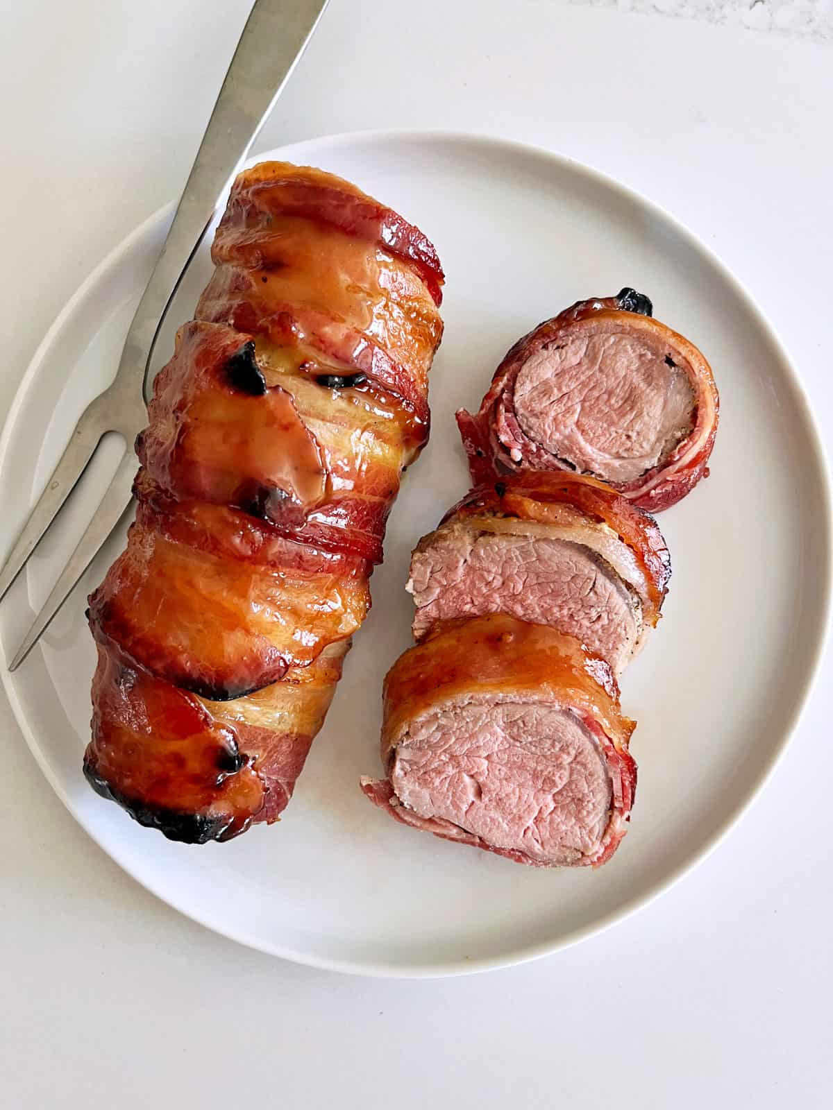 Bacon-wrapped pork tenderloin is served on a white plate.