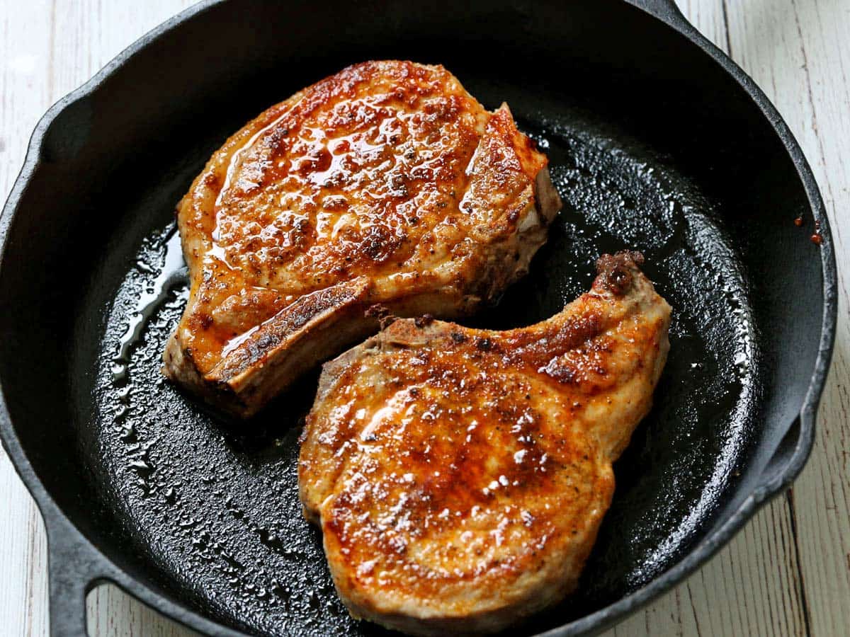 Two baked pork chops in a cast-iron skillet.