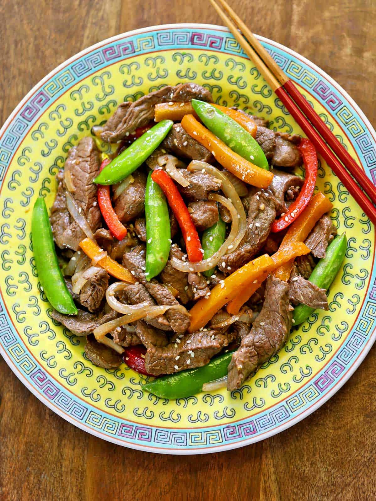 A beef stir-fry is served on a Chinese plate with chopsticks.