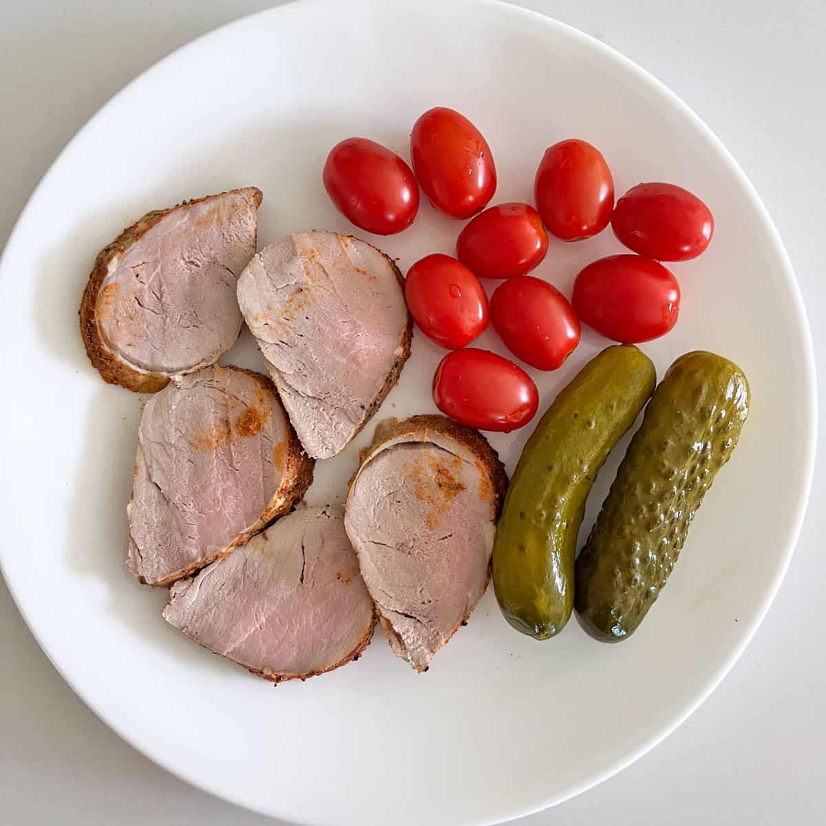 Roasted pork tenderloin leftovers are served with cherry tomatoes and dill pickles.