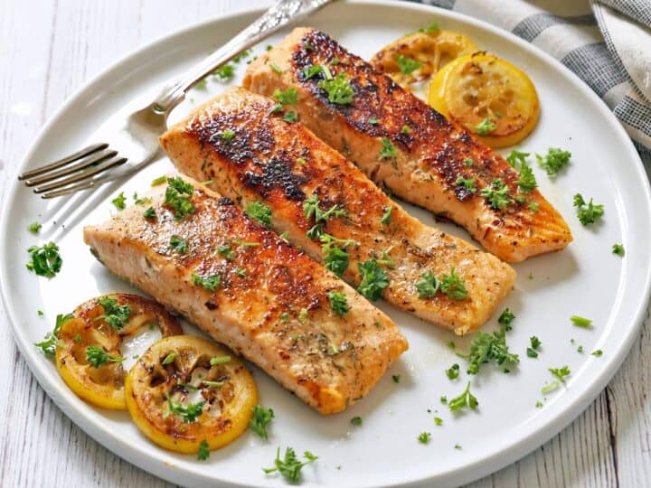 Three pieces of pan-seared salmon are served on a white plate with a fork.