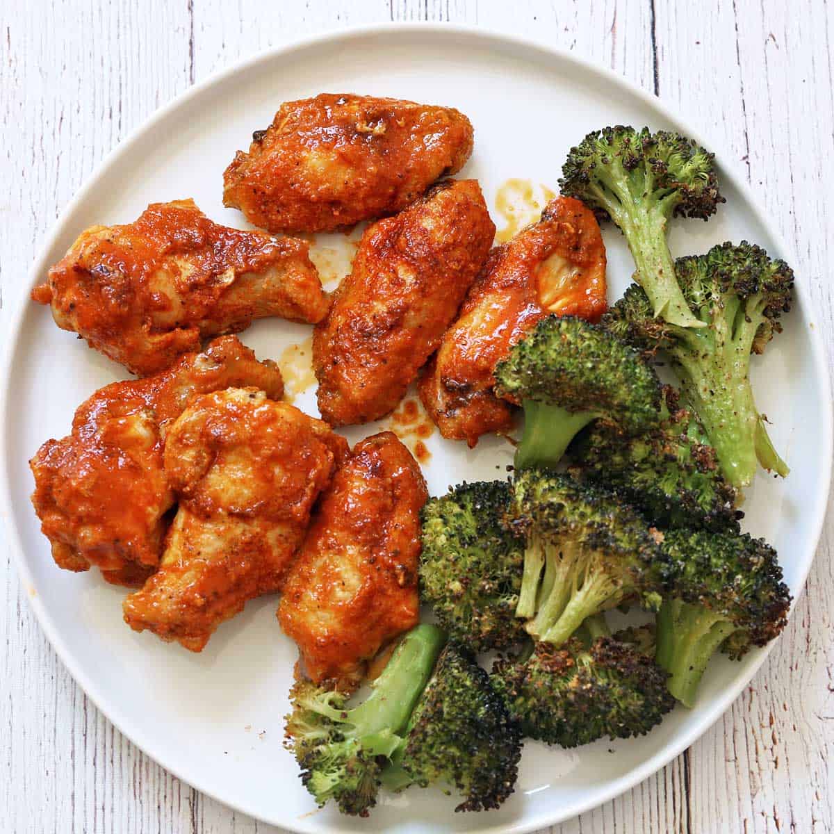 Buffalo wings are served with a side of roasted broccoli.