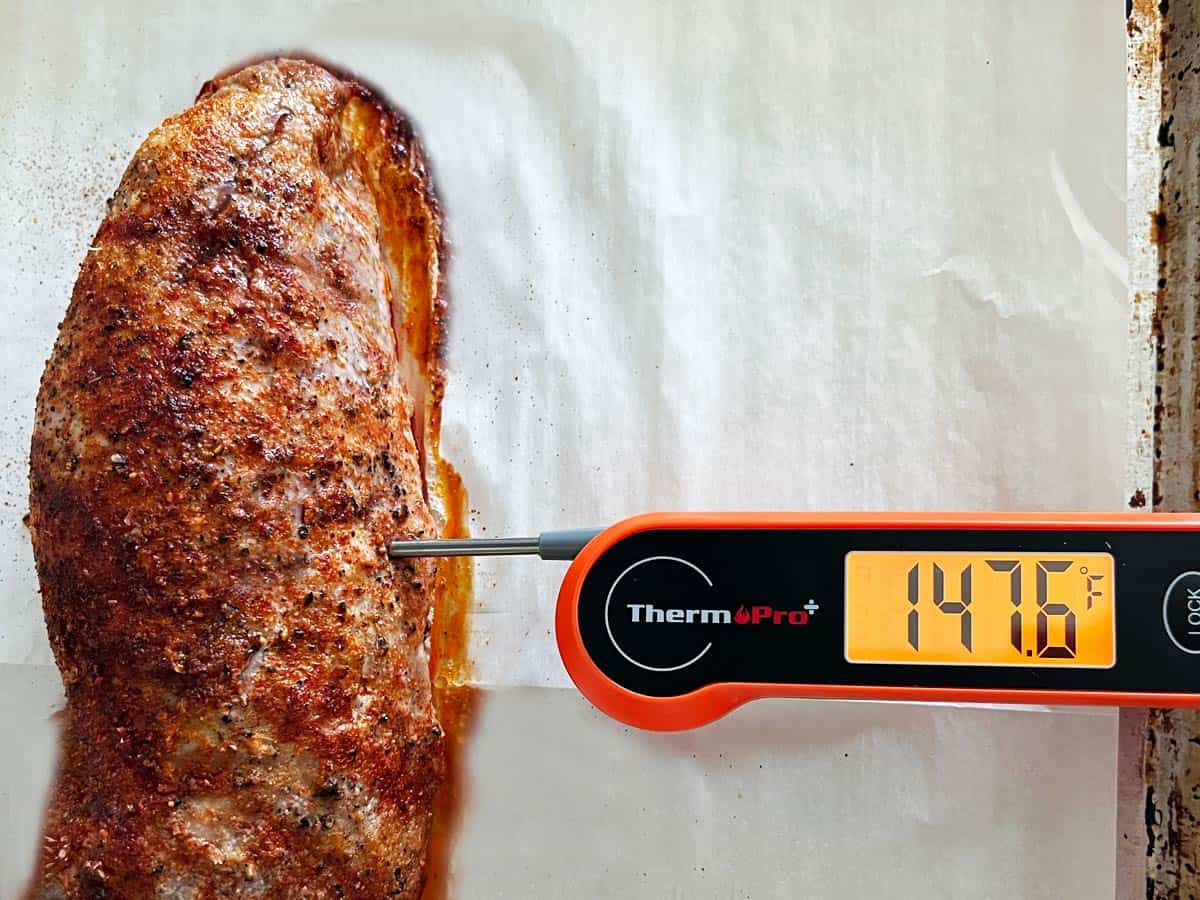 A roasted pork tenderloin with an instant-read thermometer showing an internal temperature of 147.6°F.