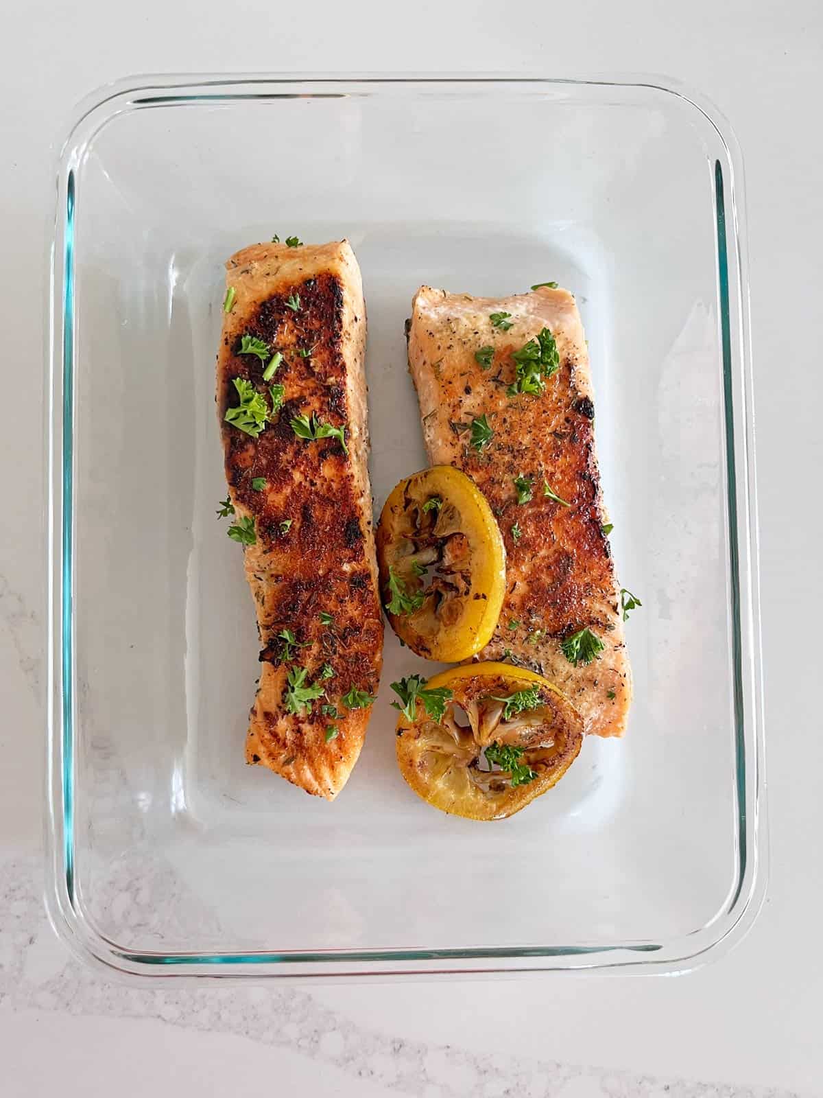 Pan-seared salmon leftovers are stored in a glass food storage container.