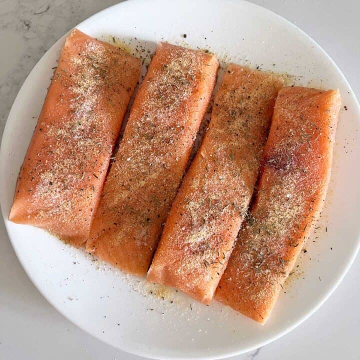 Four seasoned salmon fillets on a white plate.