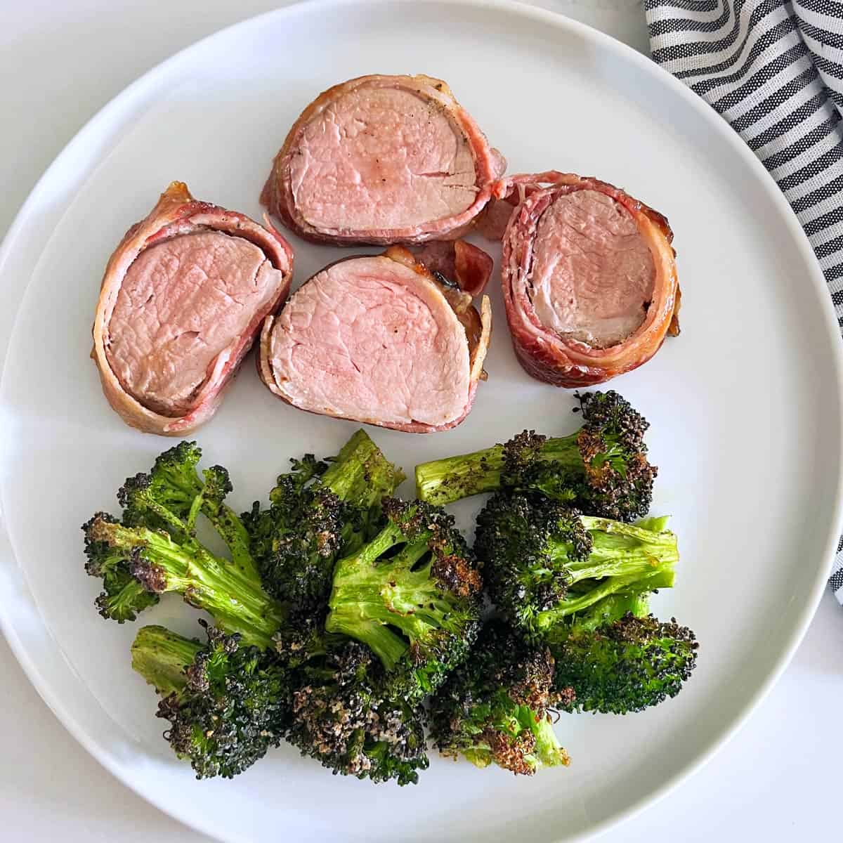 Bacon-wrapped pork tenderloin is served with roasted broccoli.