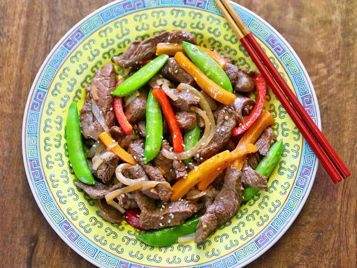 A steak stir-fry is served on a Chinese plate with chopsticks.