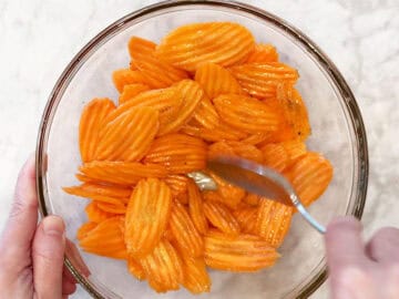 Tossing the carrot slices with oil and spices in a bowl.