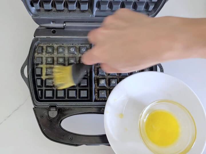 Greasing the waffle iron with melted butter.