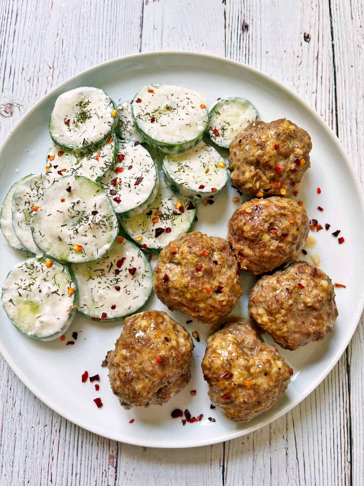 Creamy cucumber salad is served as a side dish to meatballs.
